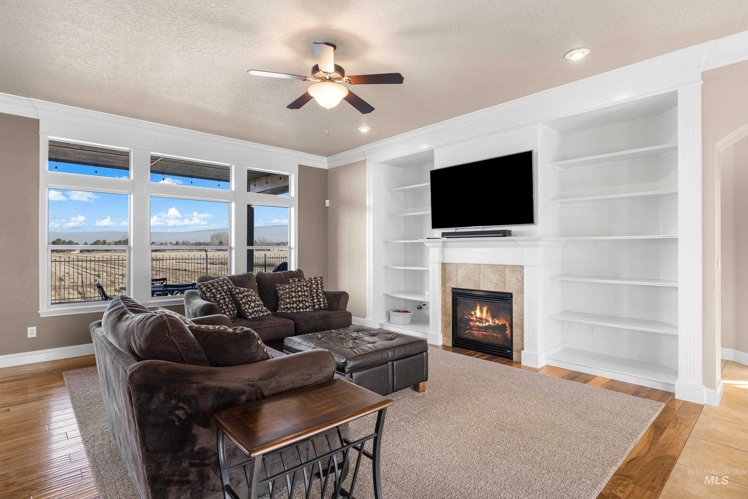 Living room featuring built in features, a tiled fireplace, light wood finished floors, a textured ceiling, and ceiling fan