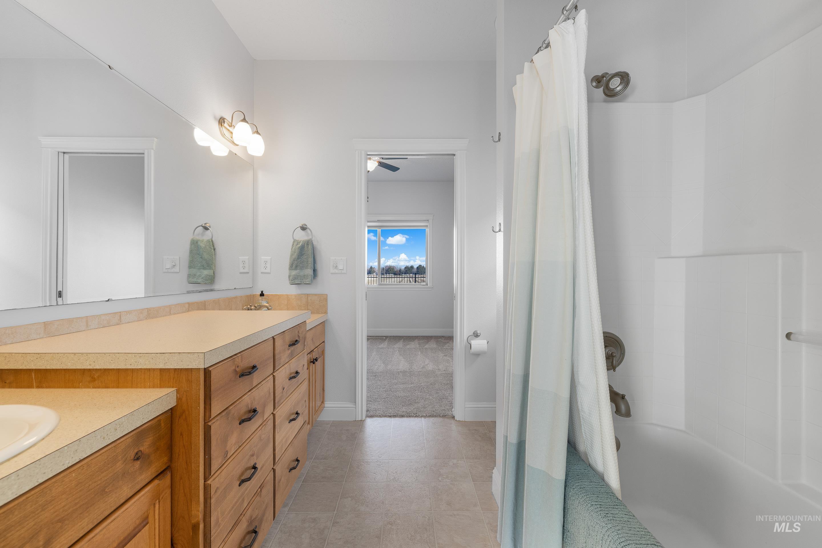 Bathroom with double vanity, shower / bath combination with curtain, a ceiling fan, and light tile patterned floors