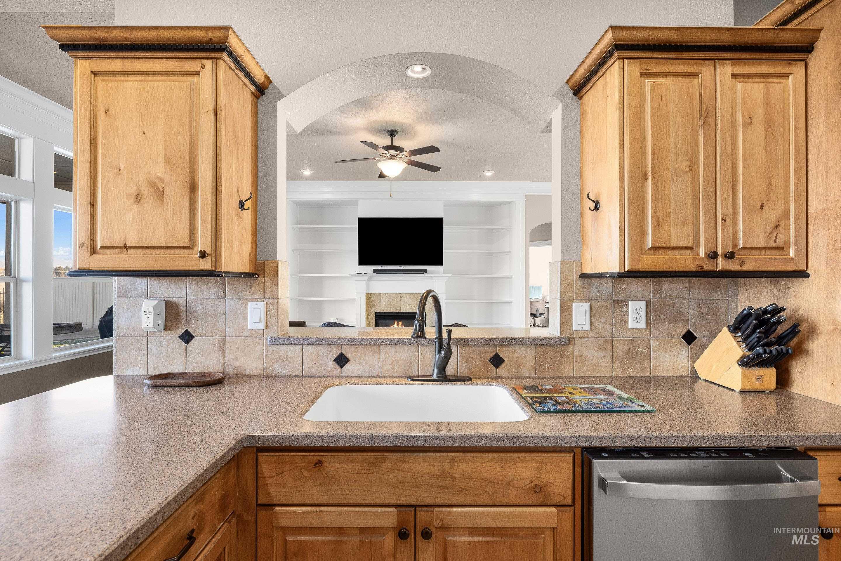 Kitchen with dishwasher, decorative backsplash, dark stone counters, and a ceiling fan
