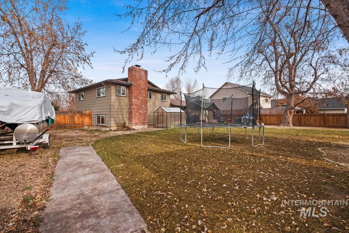 View of side of home featuring a trampoline, a fenced backyard, and a chimney