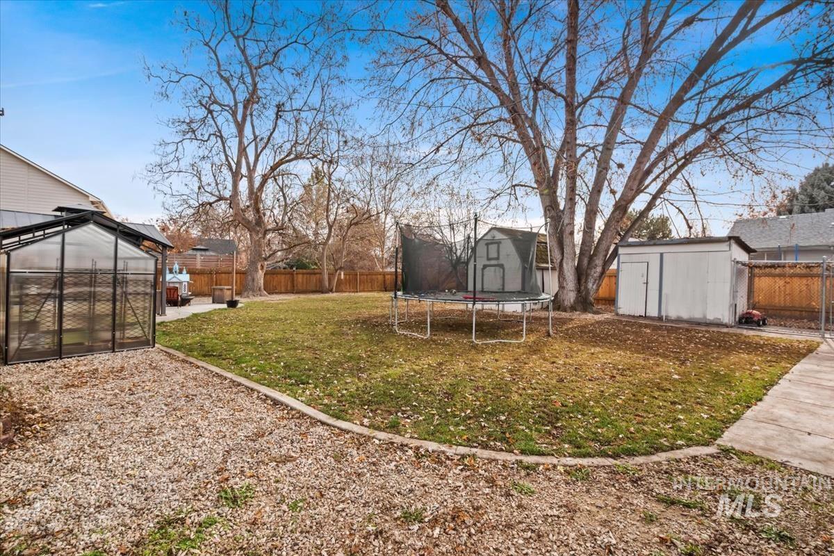Fenced backyard featuring a storage shed, a greenhouse, and a trampoline