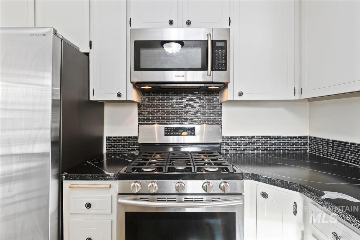 Kitchen featuring stainless steel appliances, dark countertops, white cabinets, and backsplash