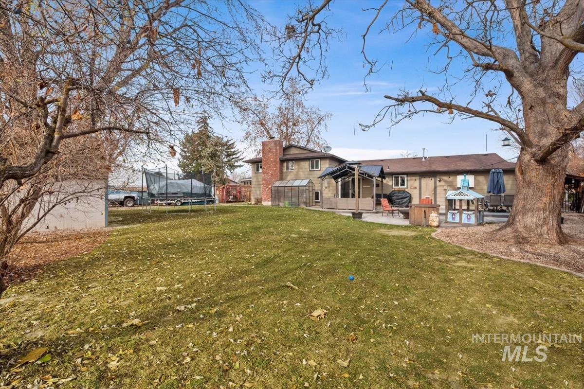 Rear view of house featuring a trampoline, a lawn, a chimney, a patio, and a gazebo