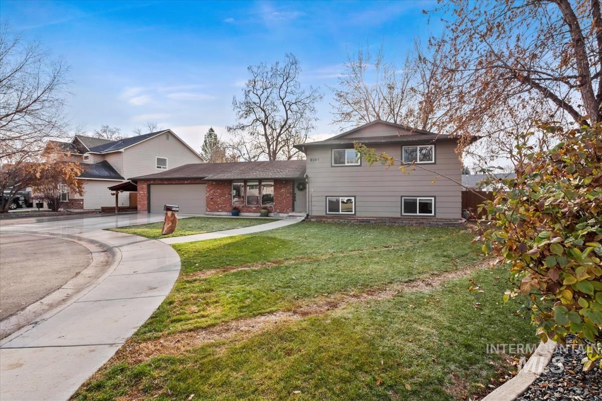 Split level home featuring a front lawn, concrete driveway, a garage, and brick siding