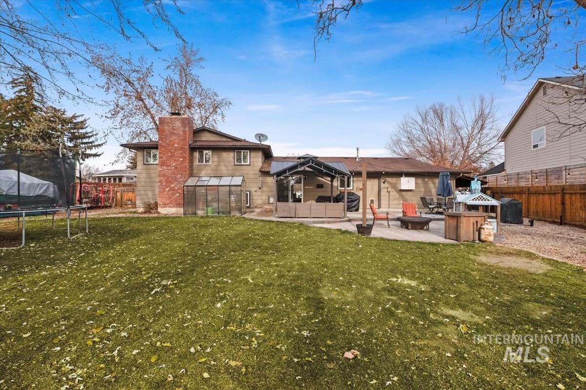 Rear view of house featuring a chimney, a trampoline, a fenced backyard, and a patio area