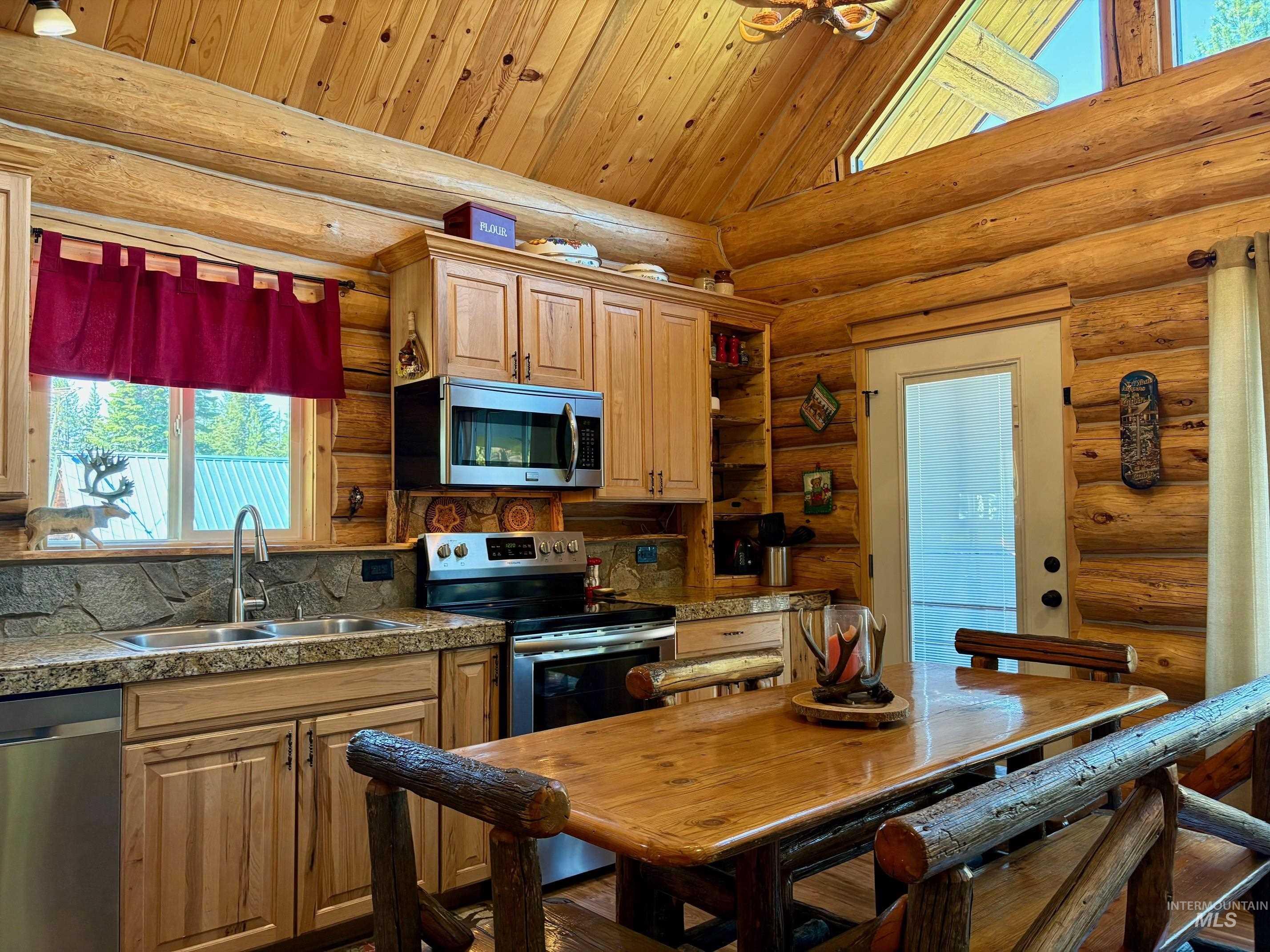 Kitchen featuring plenty of natural light, appliances with stainless steel finishes, tile countertops, high vaulted ceiling, and log walls