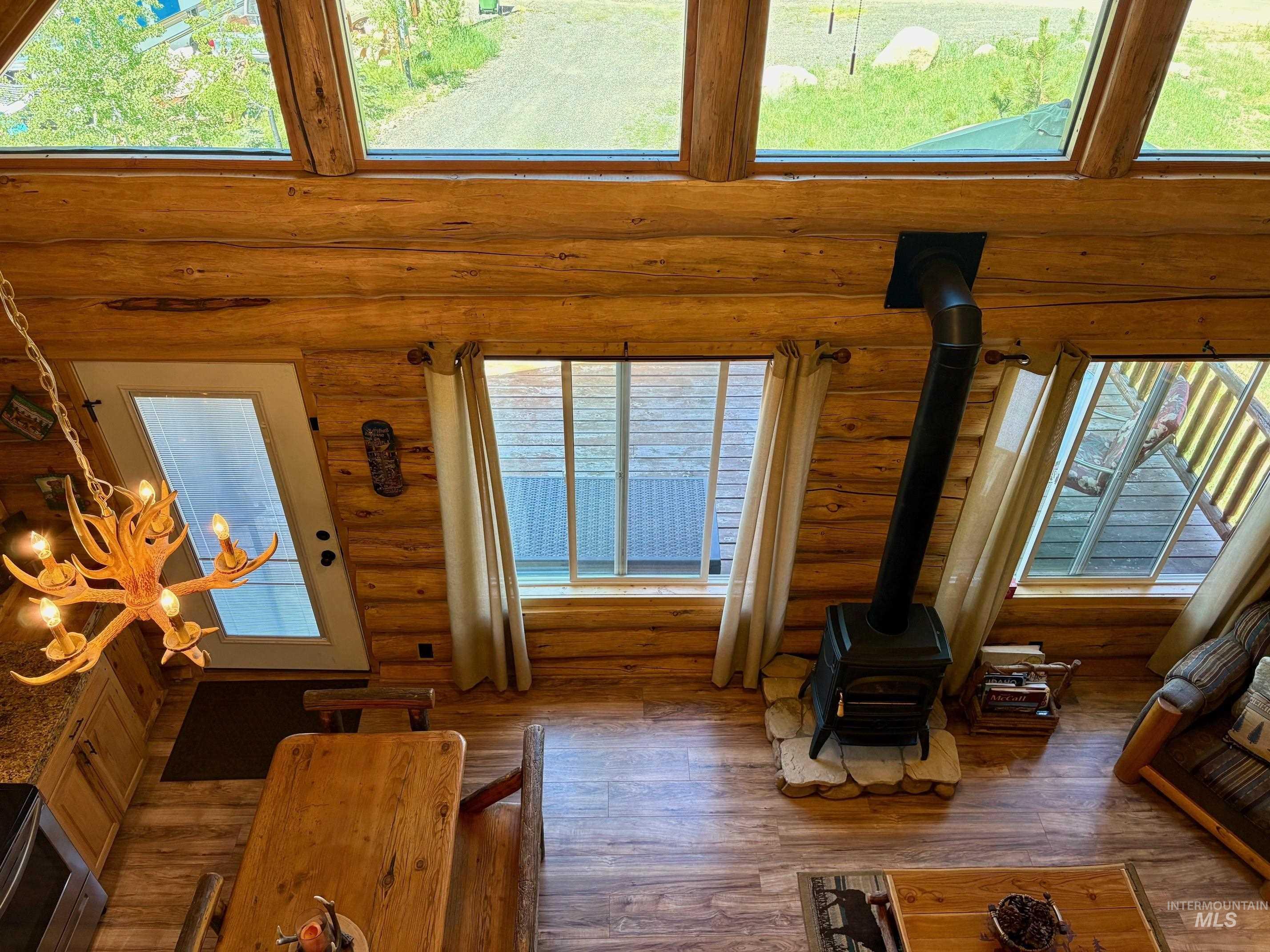Living area featuring a wood stove, log walls, wood-type flooring, and a high ceiling
