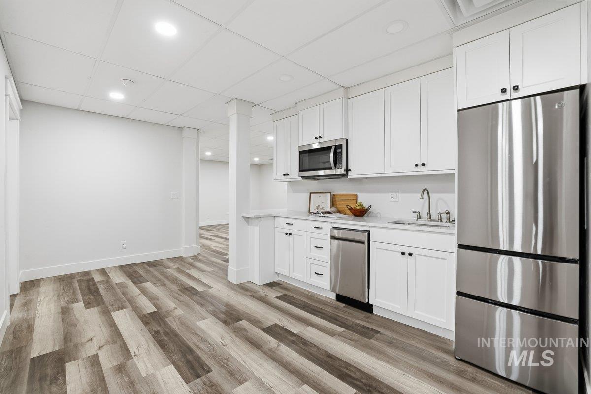 Kitchen featuring stainless steel appliances, white cabinetry, a paneled ceiling, light wood-style floors, and recessed lighting, Fridge, dishwasher and microwave.