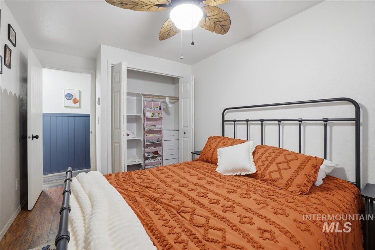 Bedroom with a closet, ceiling fan, wood finished floors, and wainscoting