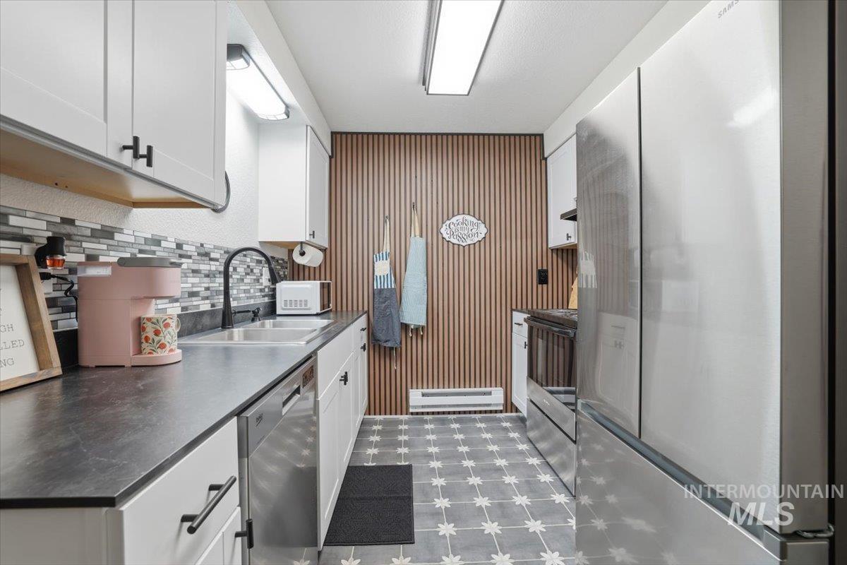 Kitchen featuring stainless steel appliances, white cabinets, dark floors, dark countertops, and baseboard heating