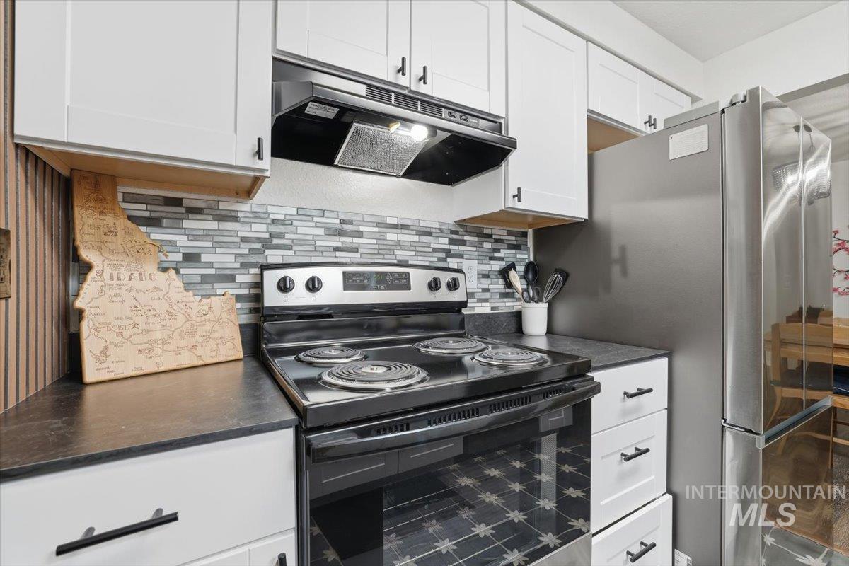 Kitchen featuring black range with electric stovetop, white cabinetry, dark countertops, backsplash, and freestanding refrigerator