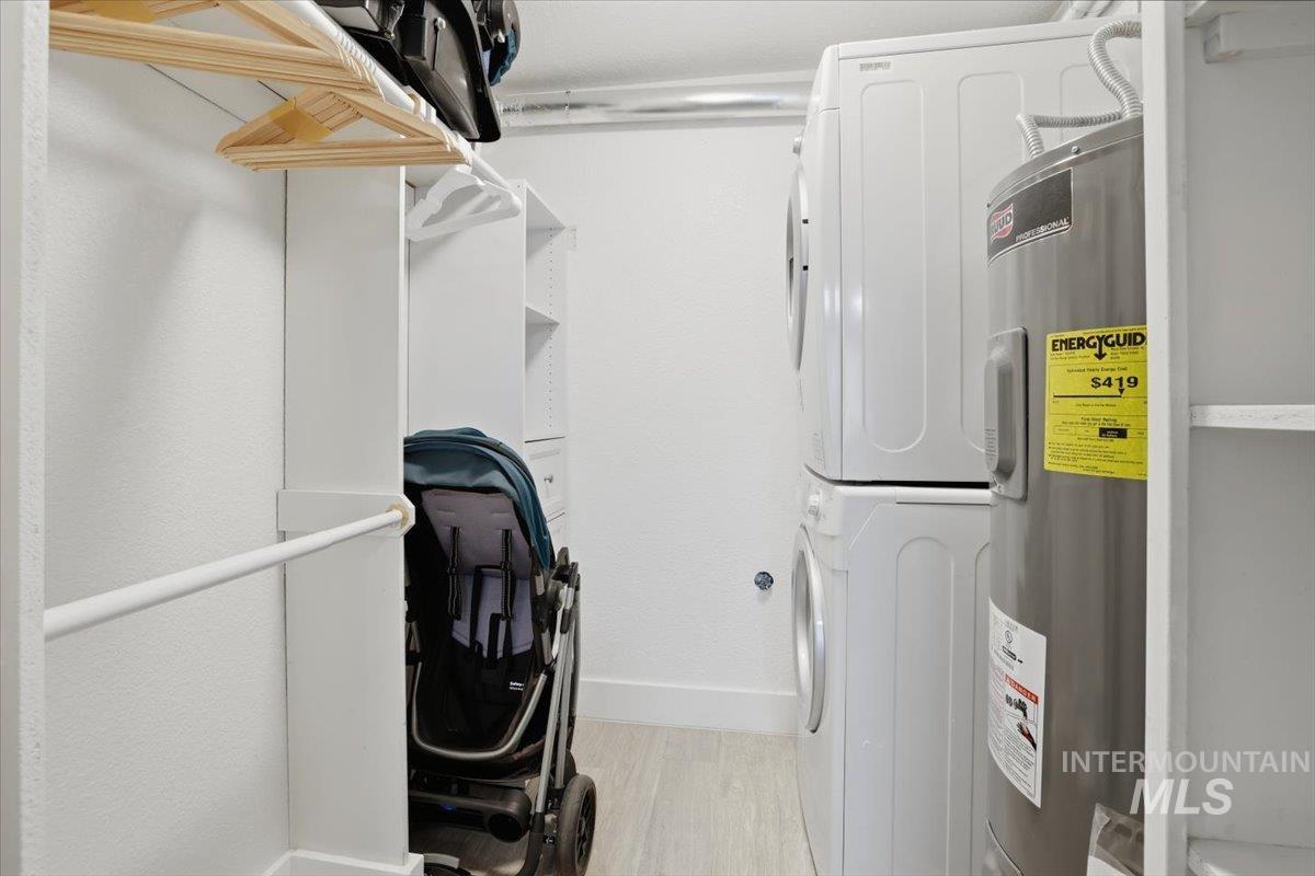Laundry area featuring electric water heater, stacked washer / dryer, and light wood finished floors
