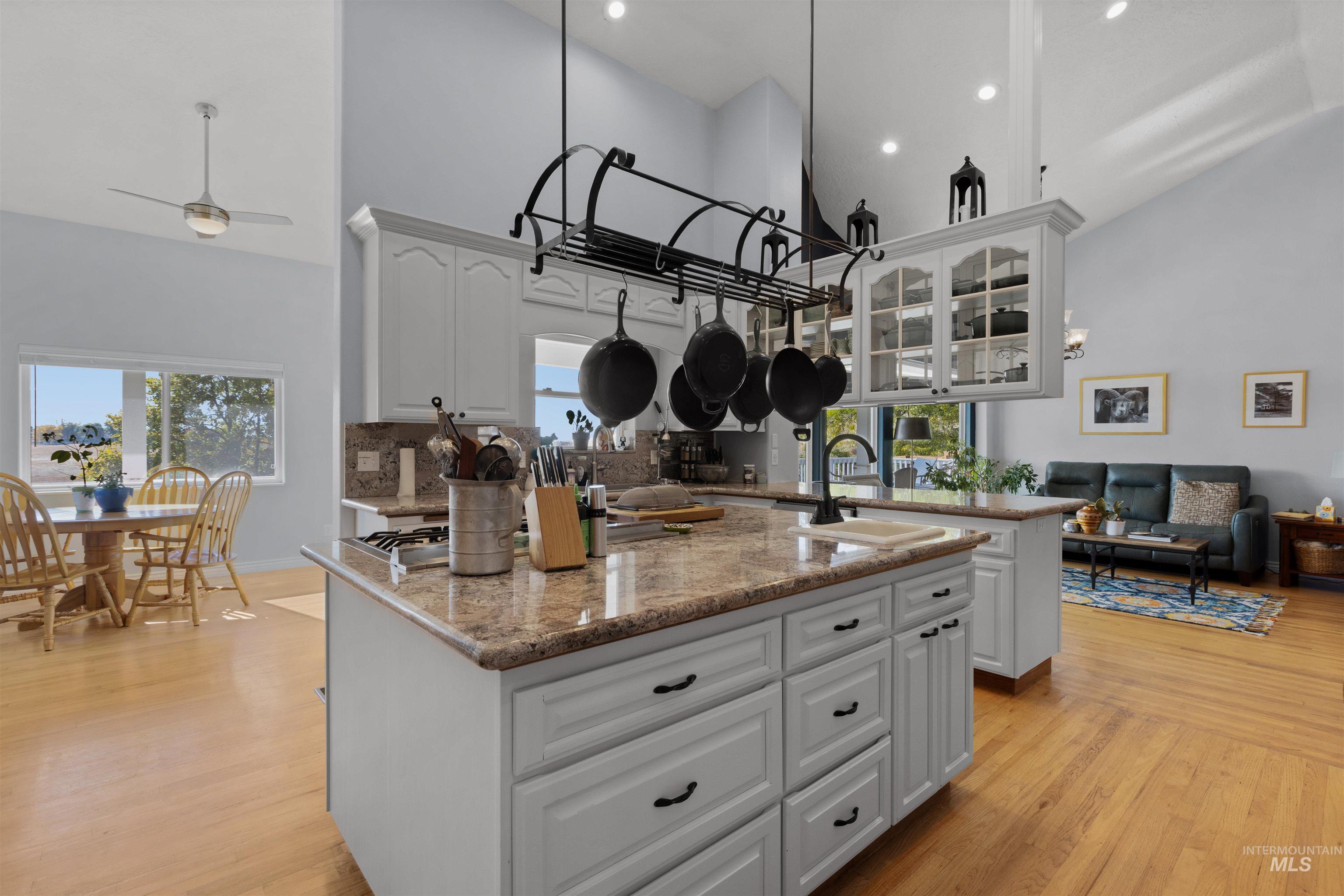Kitchen featuring high vaulted ceiling, a center island with sink, light stone counters, white cabinetry, and light wood-type flooring