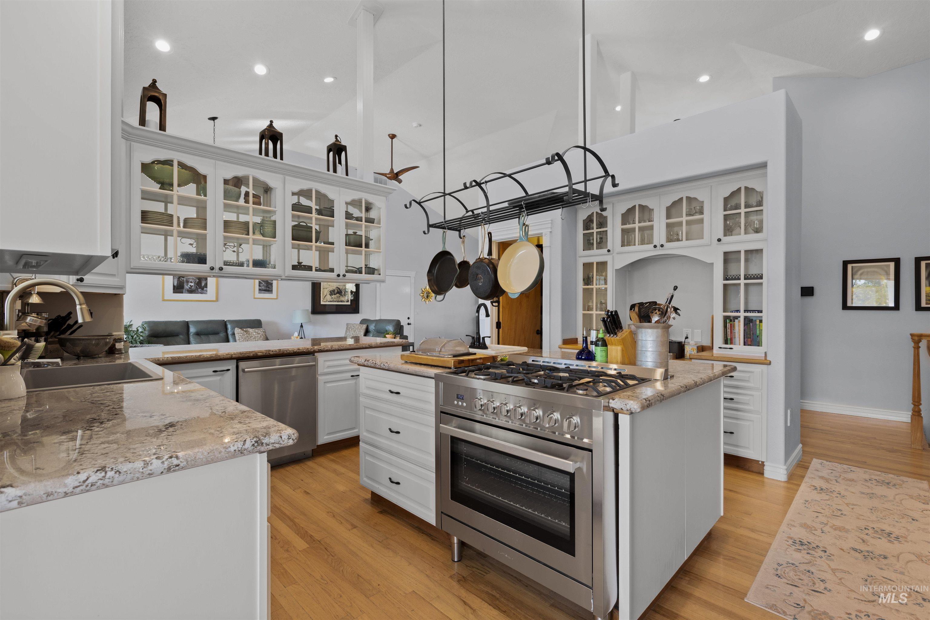 Kitchen featuring white cabinetry, glass insert cabinets, appliances with stainless steel finishes, light stone counters, and light wood-style flooring