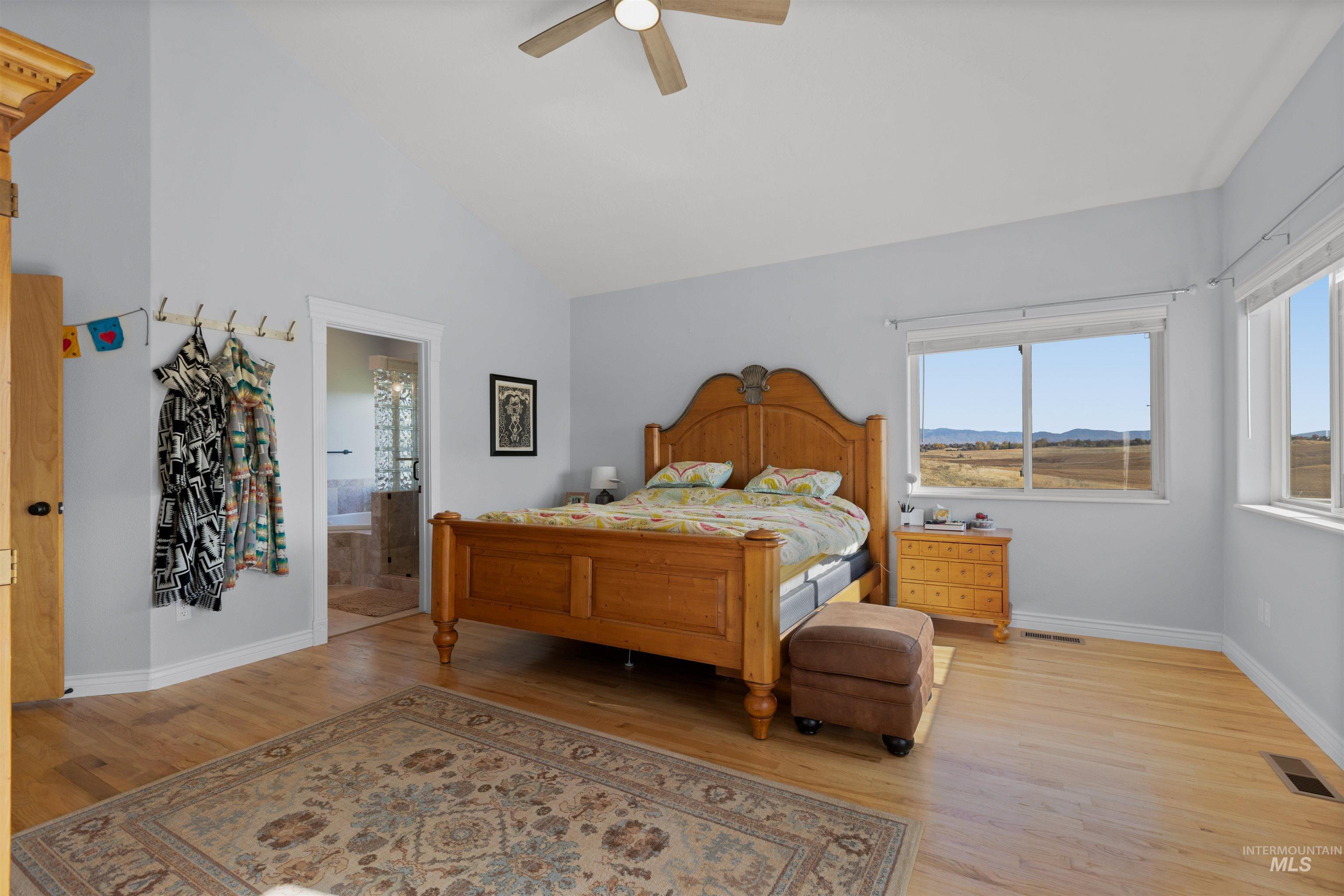 Bedroom with light wood-type flooring, high vaulted ceiling, ceiling fan, and ensuite bathroom