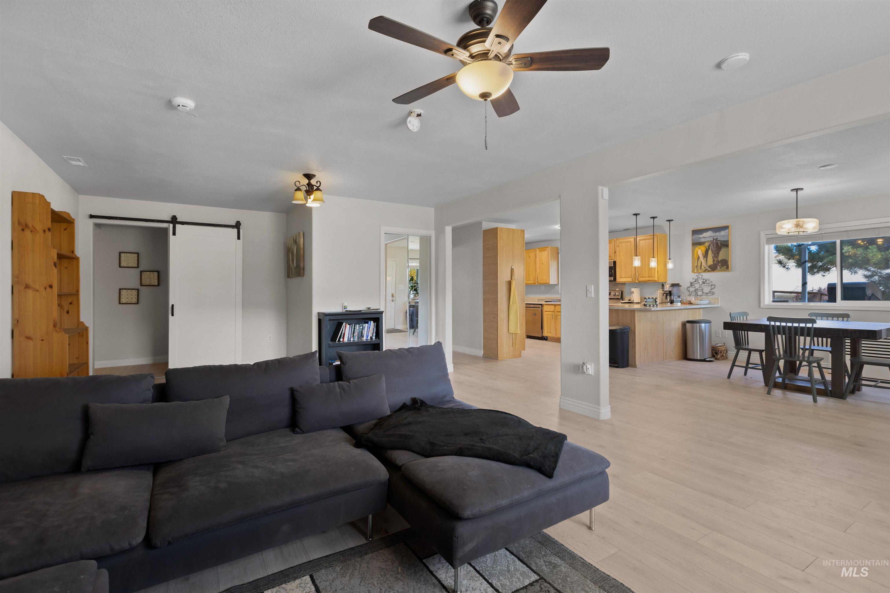 Living room featuring a barn door, light wood-style flooring, and ceiling fan