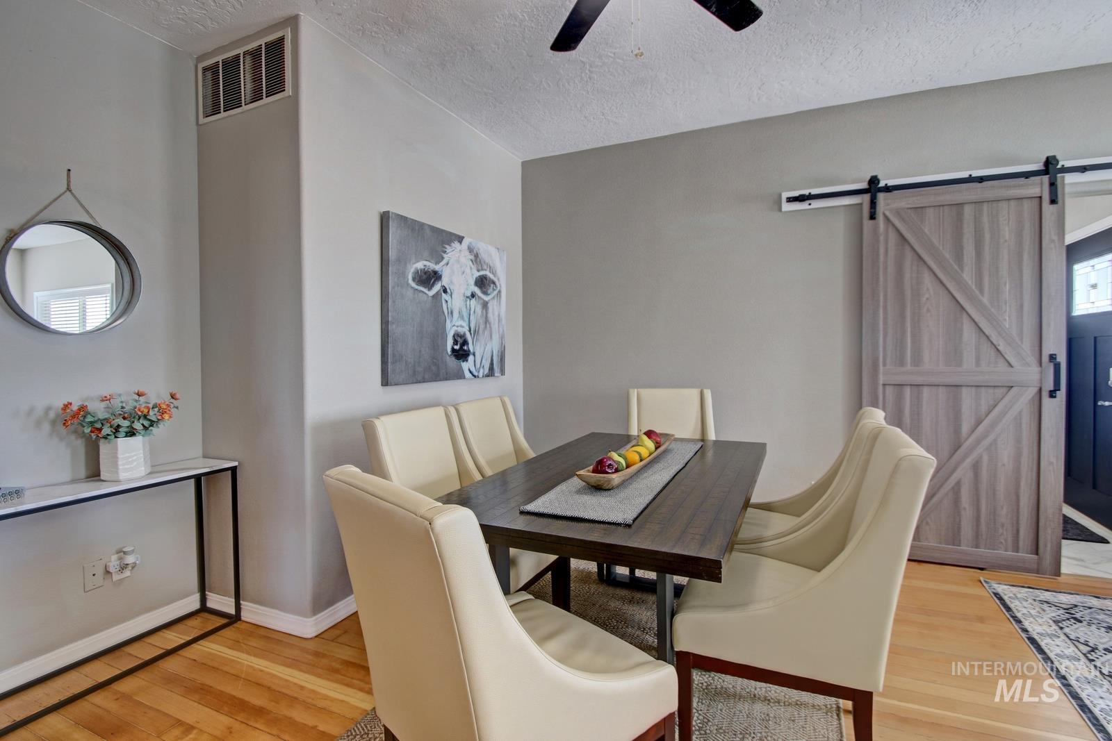 Dining room featuring a barn door, light wood-type flooring, a textured ceiling, and ceiling fan