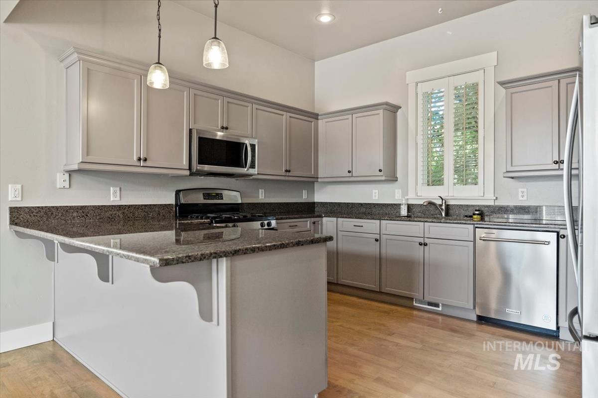 Kitchen with a peninsula, appliances with stainless steel finishes, dark stone counters, gray cabinets, and decorative light fixtures
