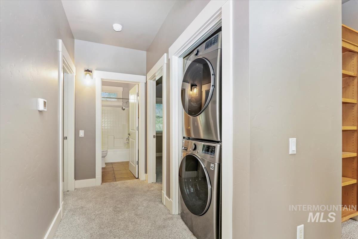 Laundry area featuring light colored carpet and stacked washer / drying machine