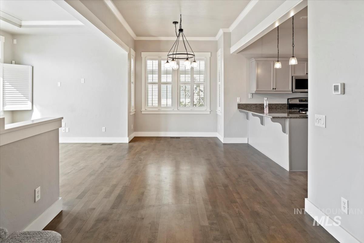 Unfurnished dining area featuring dark wood-style floors and ornamental molding