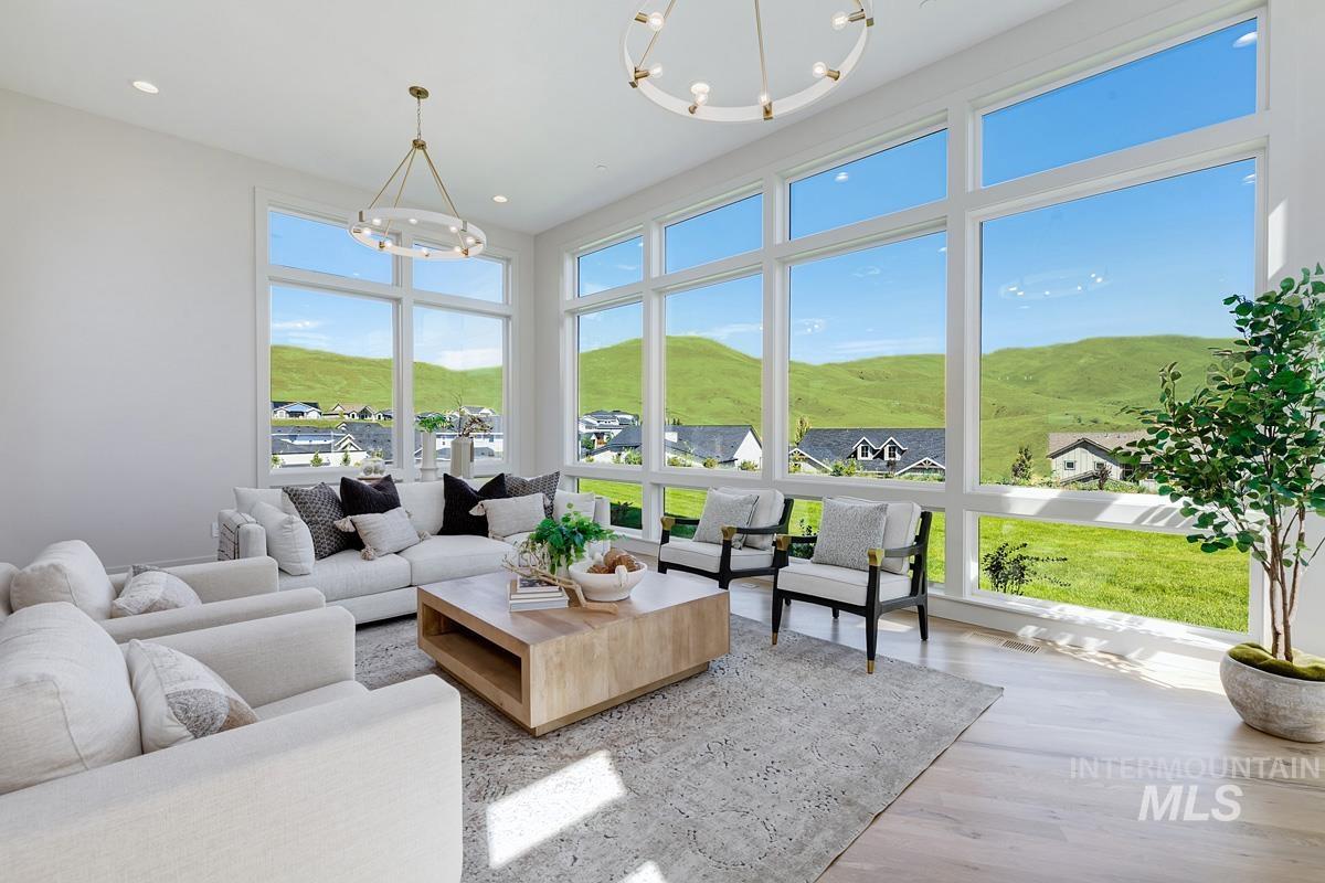 Expansive living area featuring floor-to-ceiling windows, light wood-finish flooring, and two modern brass chandeliers