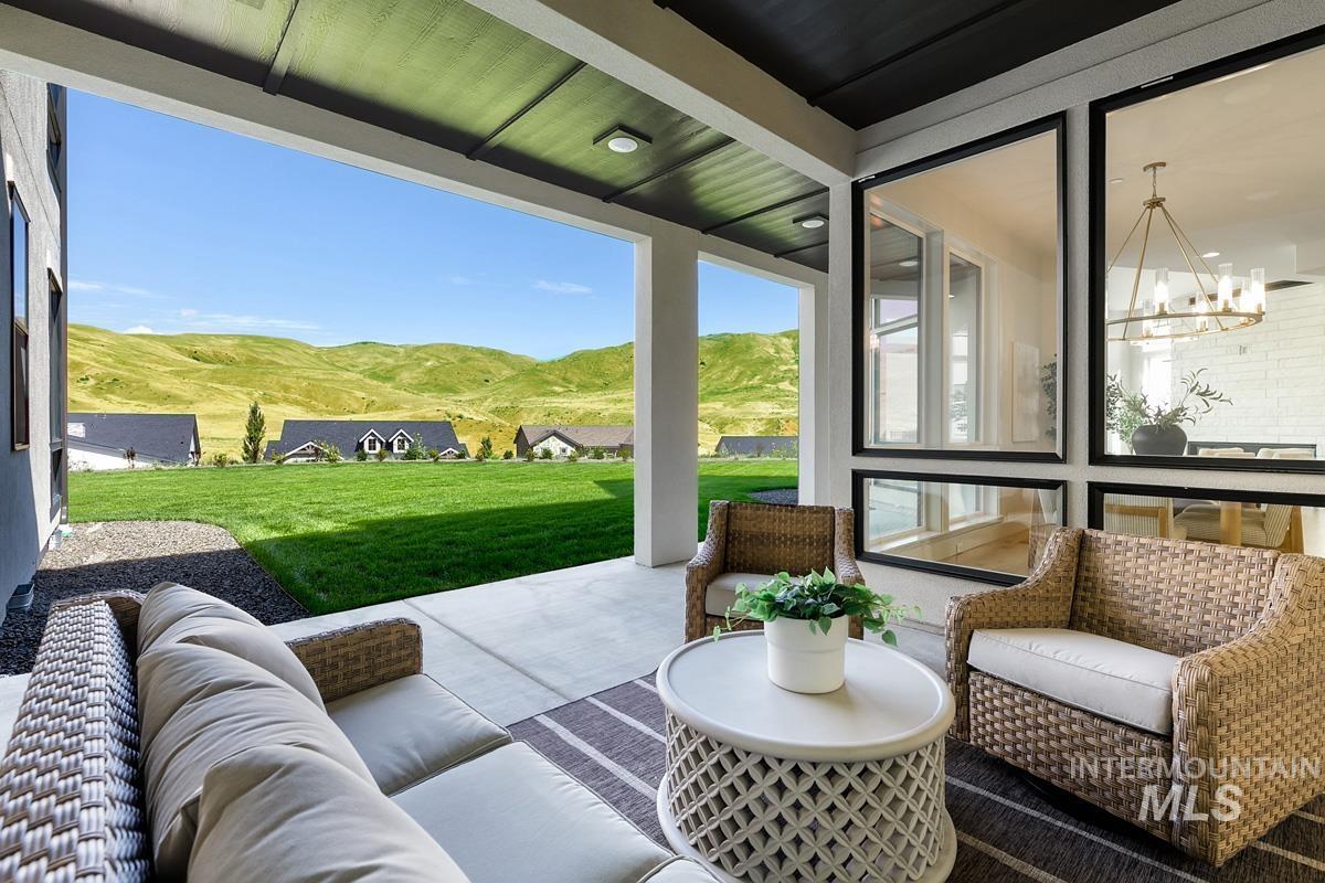 Covered patio with concrete flooring, recessed lighting, and expansive glass panels overlooking a manicured lawn and distant rolling hills
