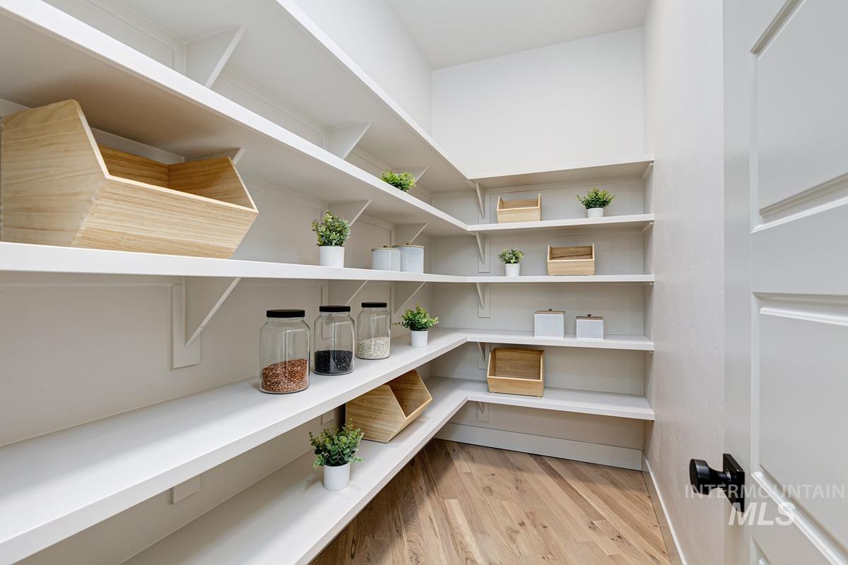 Walk-in pantry featuring extensive white shelving, wood-finish flooring, and a white paneled door with matte black hardware