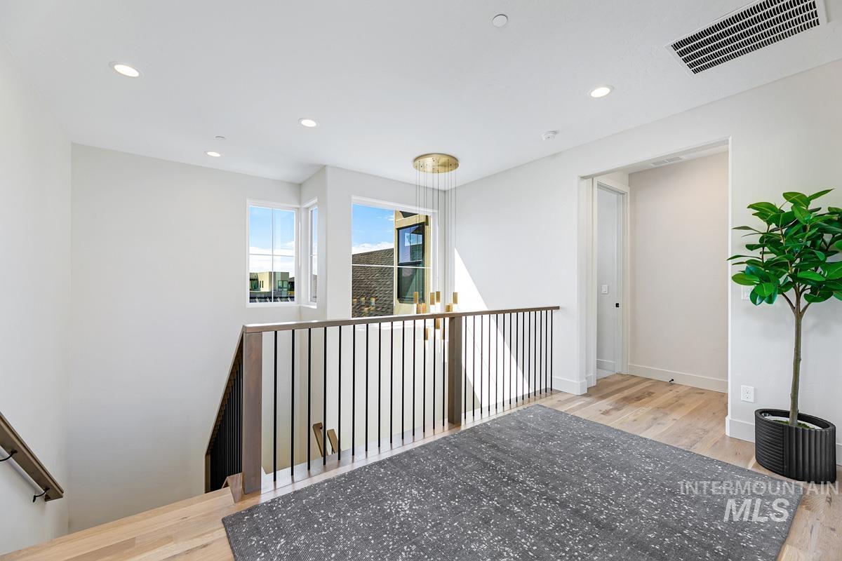 Upper-level landing featuring wood-finish flooring, a contemporary chandelier, multiple windows, recessed lighting, and a modern stair railing