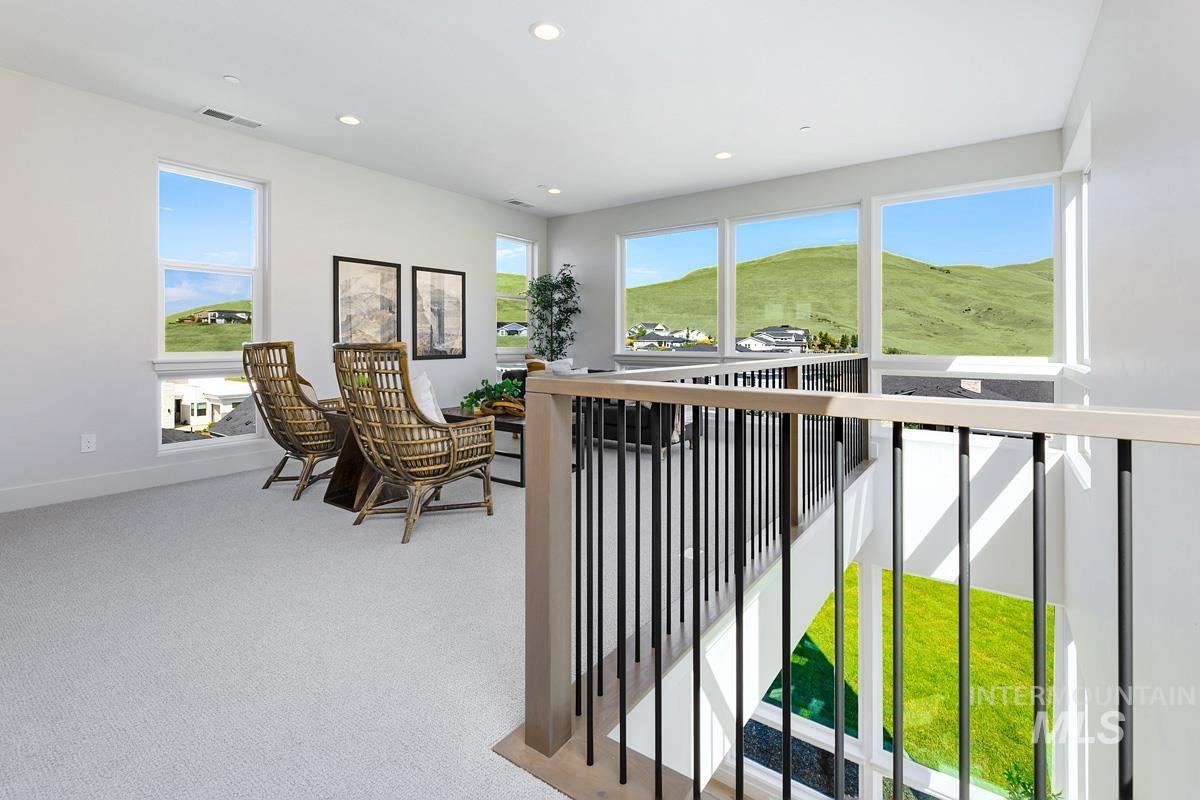 Upper-level loft space featuring light-colored carpeting, recessed lighting, white walls, and multiple large windows with scenic hill and community backdrops