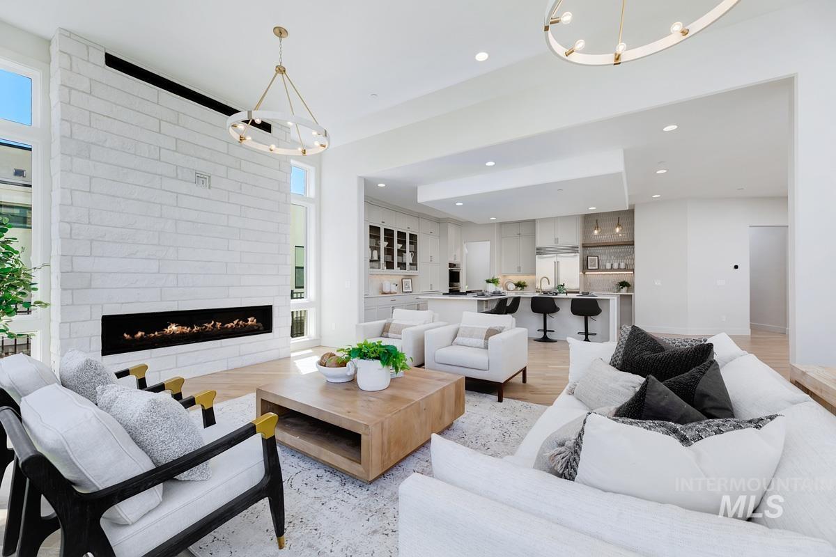 Spacious living area featuring a full-height stacked stone fireplace, wood-finish flooring, and high ceilings with contemporary chandeliers