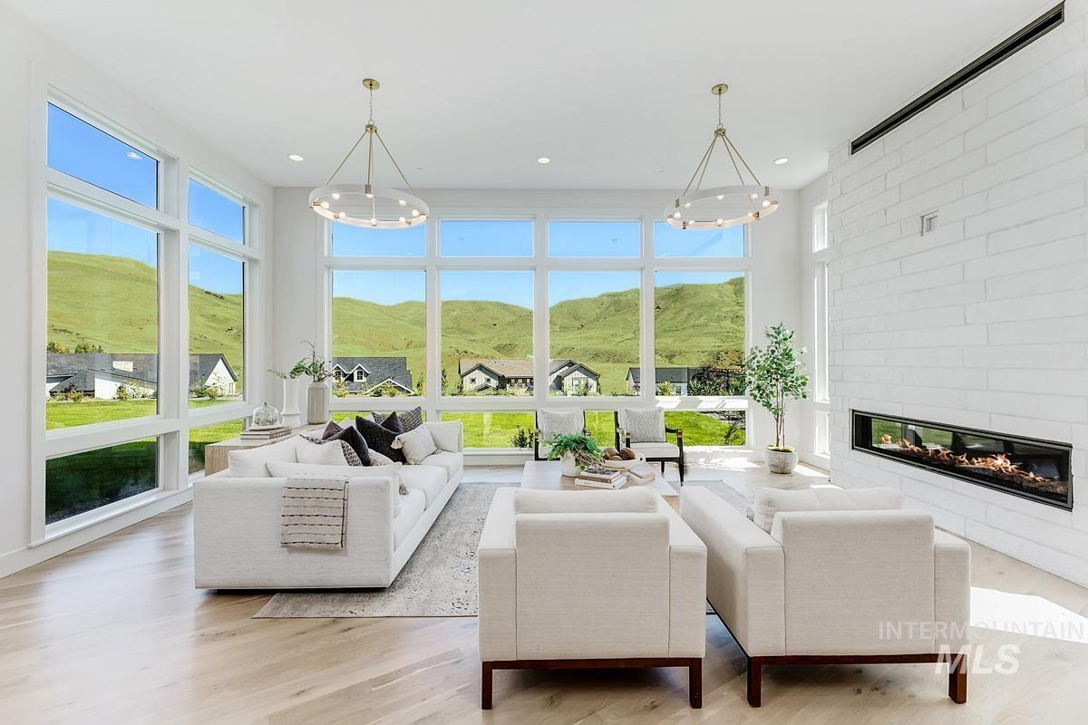 Spacious living area featuring expansive windows, wood-finish flooring, a linear electric fireplace with a stacked stone surround, and two contemporary chandeliers