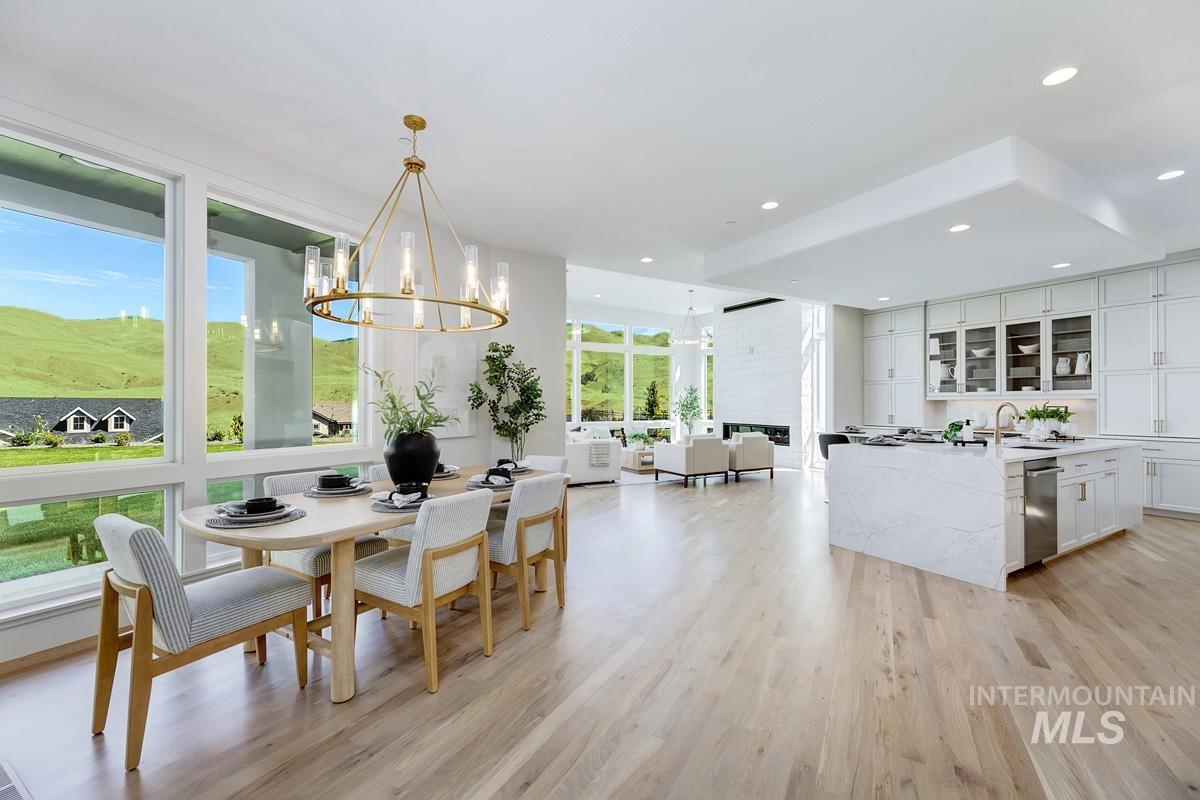 Spacious open-concept interior featuring light wood-finish flooring, a contemporary kitchen island with a waterfall countertop, white cabinetry with glass-front accents, and a modern linear fireplace
