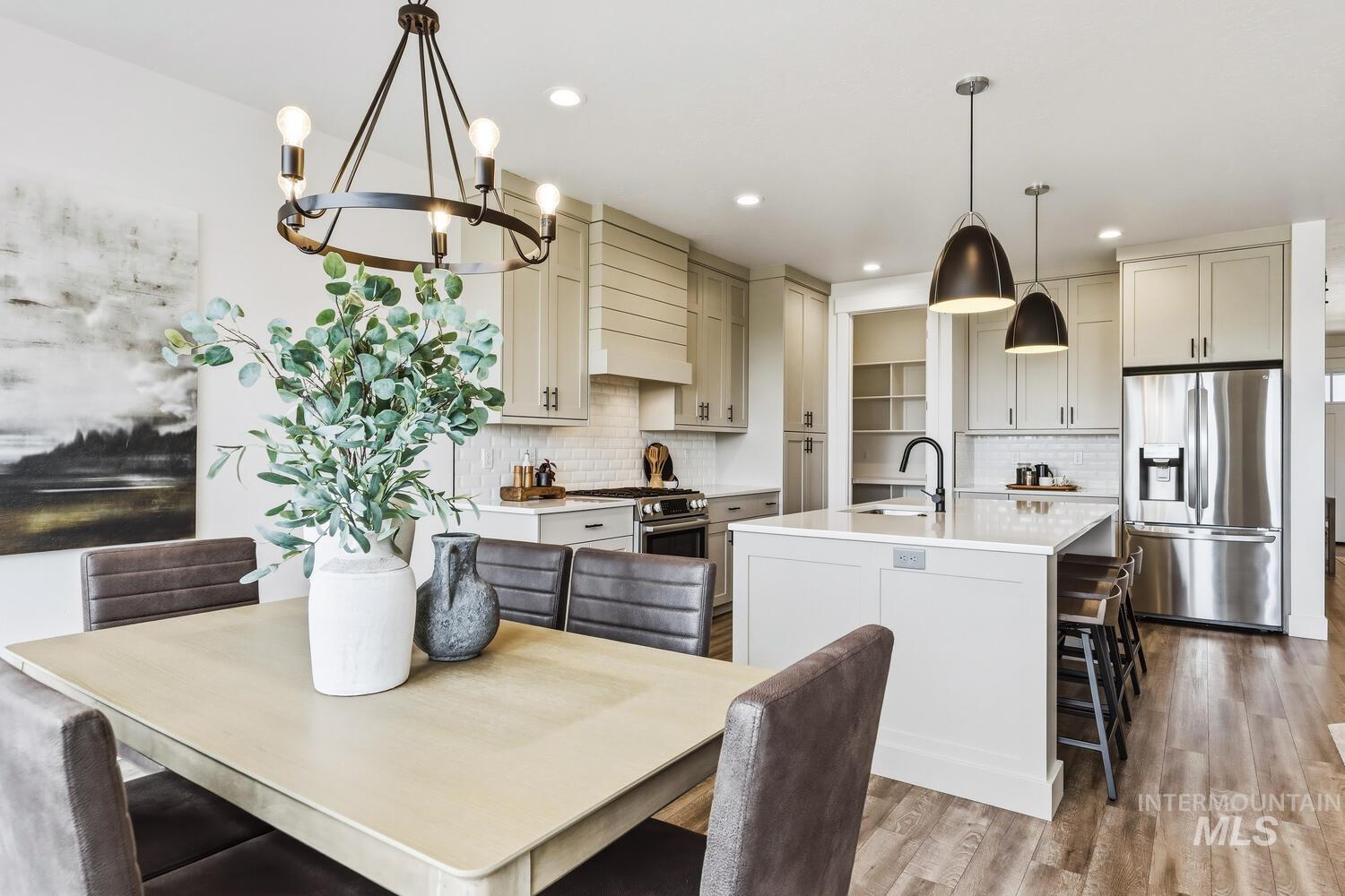 Kitchen with stainless steel appliances, suspended lighting, a kitchen island with sink, a breakfast bar area, and light wood-style floors