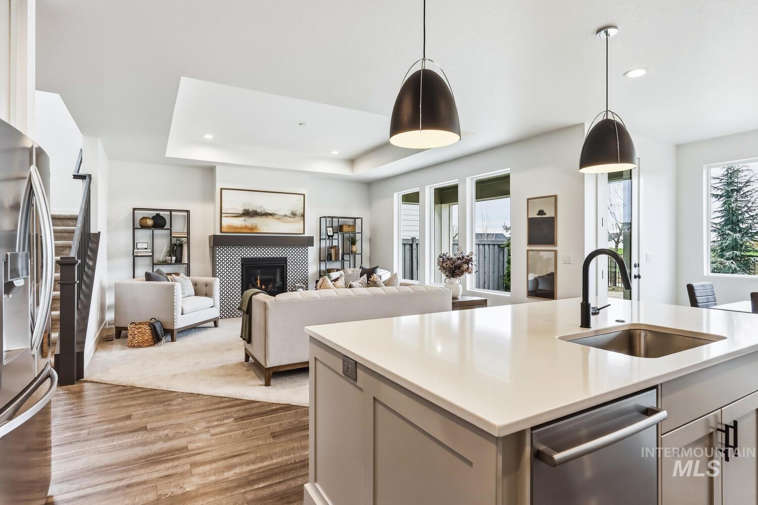 Kitchen featuring open floor plan, light wood-style floors, stainless steel appliances, hanging light fixtures, and a tile fireplace