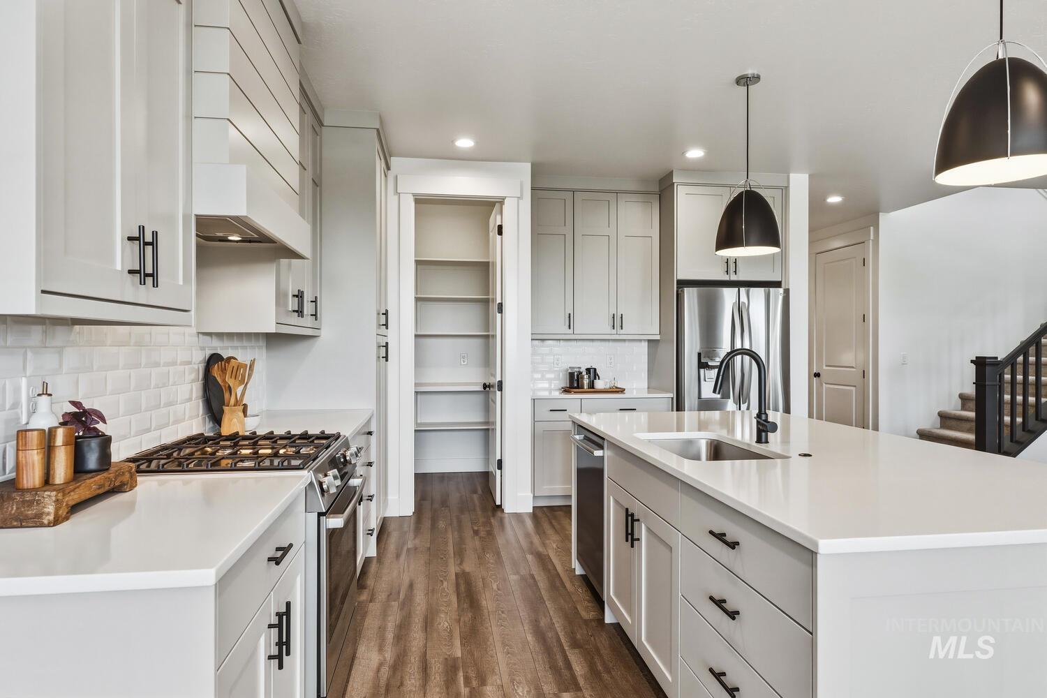 Kitchen with stainless steel appliances, a kitchen island with sink, dark wood finished floors, hanging light fixtures, and tasteful backsplash