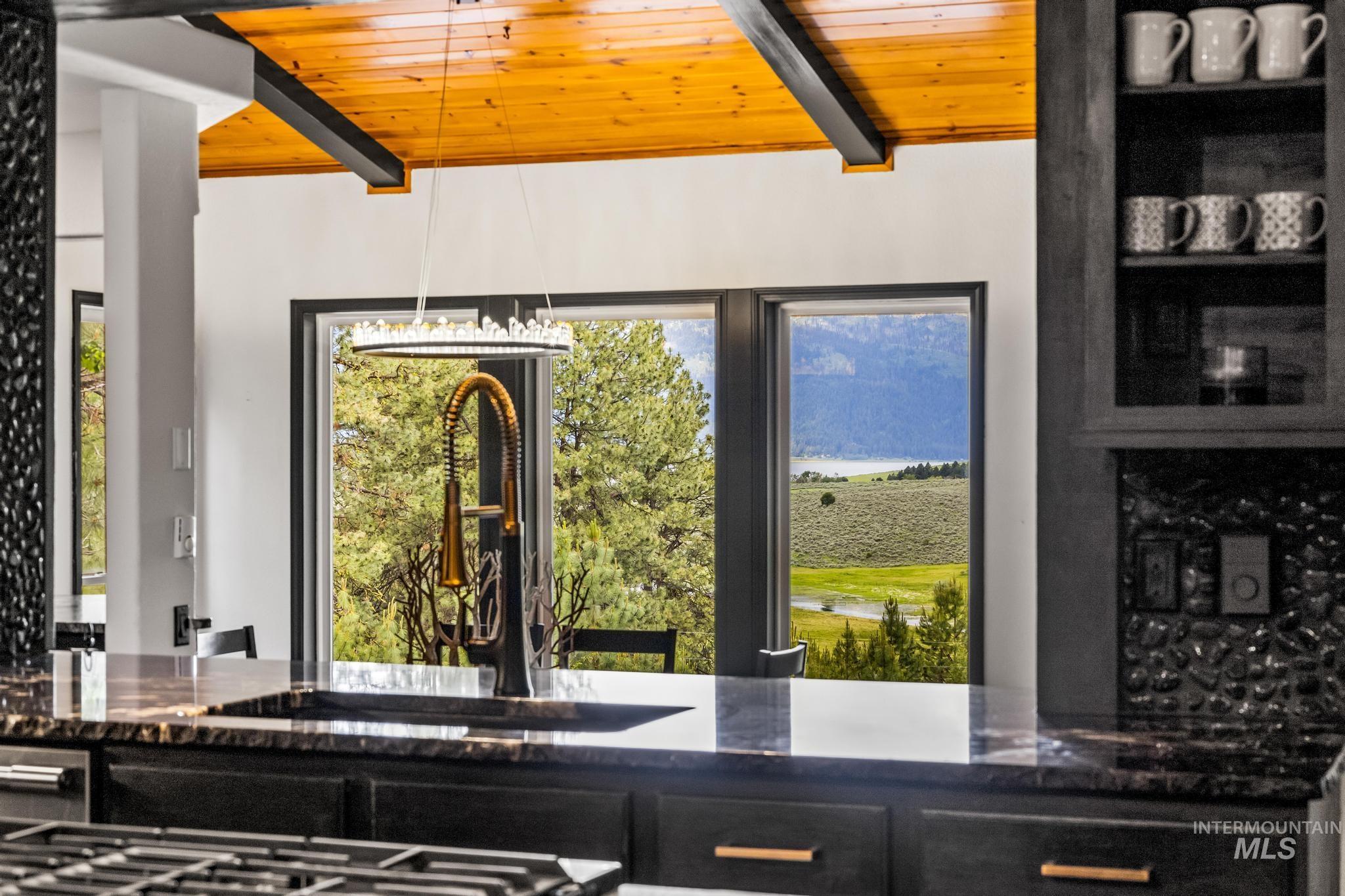 Kitchen view of dark stone countertops, dark cabinets, a wood ceiling with exposed beams, and glass insert cabinets