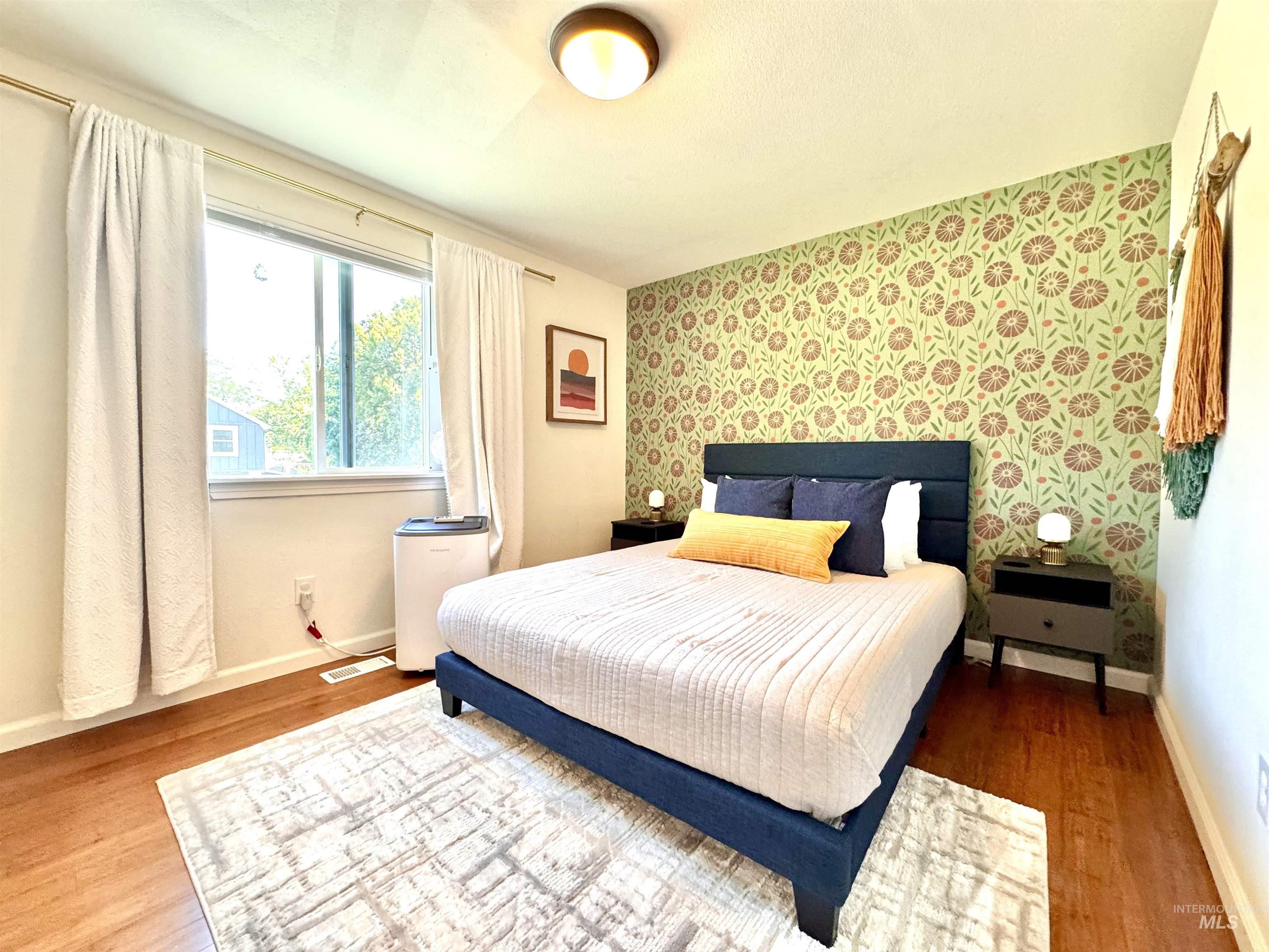 Bedroom featuring wallpapered walls, an accent wall, and wood finished floors