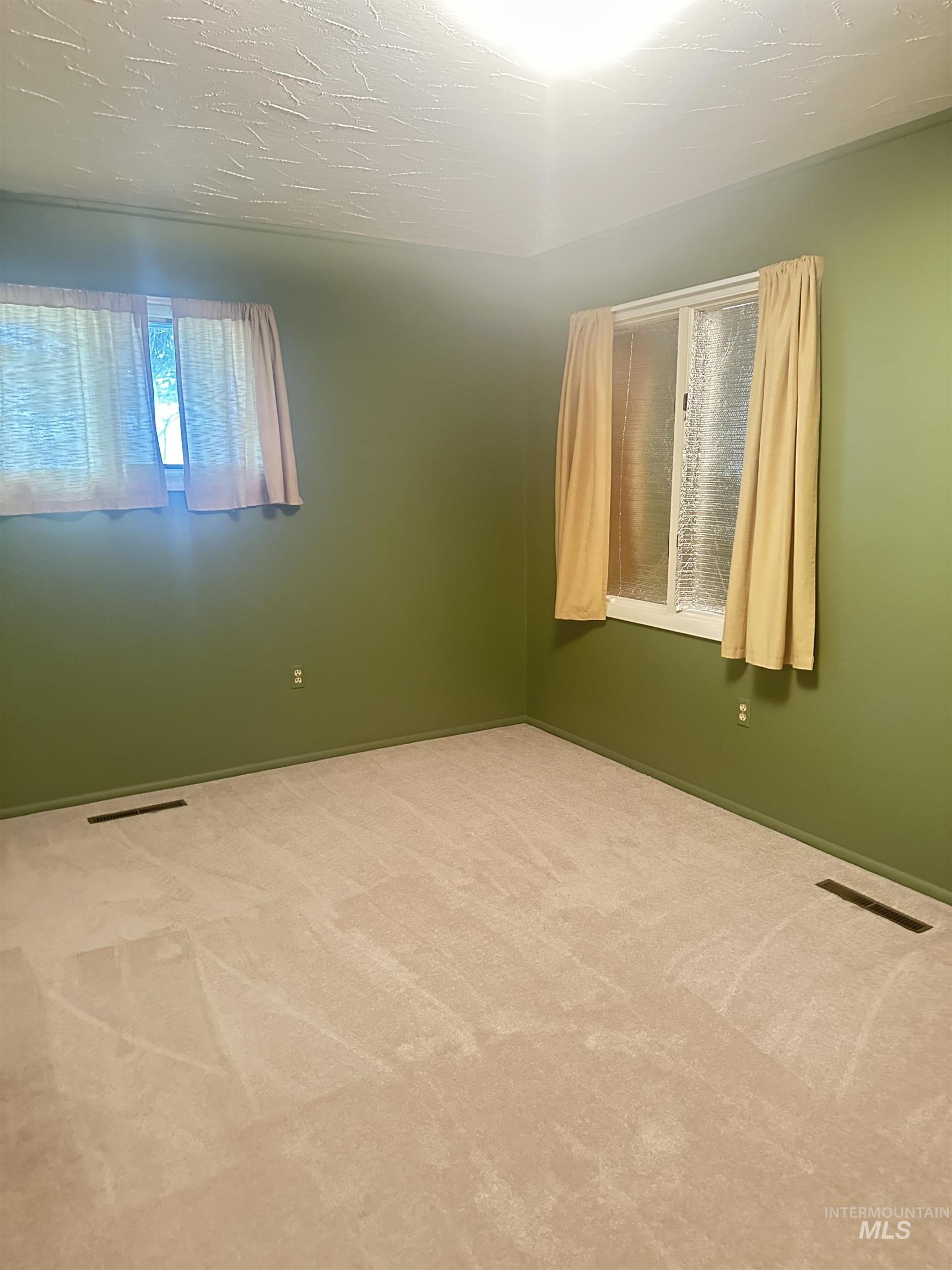Carpeted spare room featuring a textured ceiling and baseboards