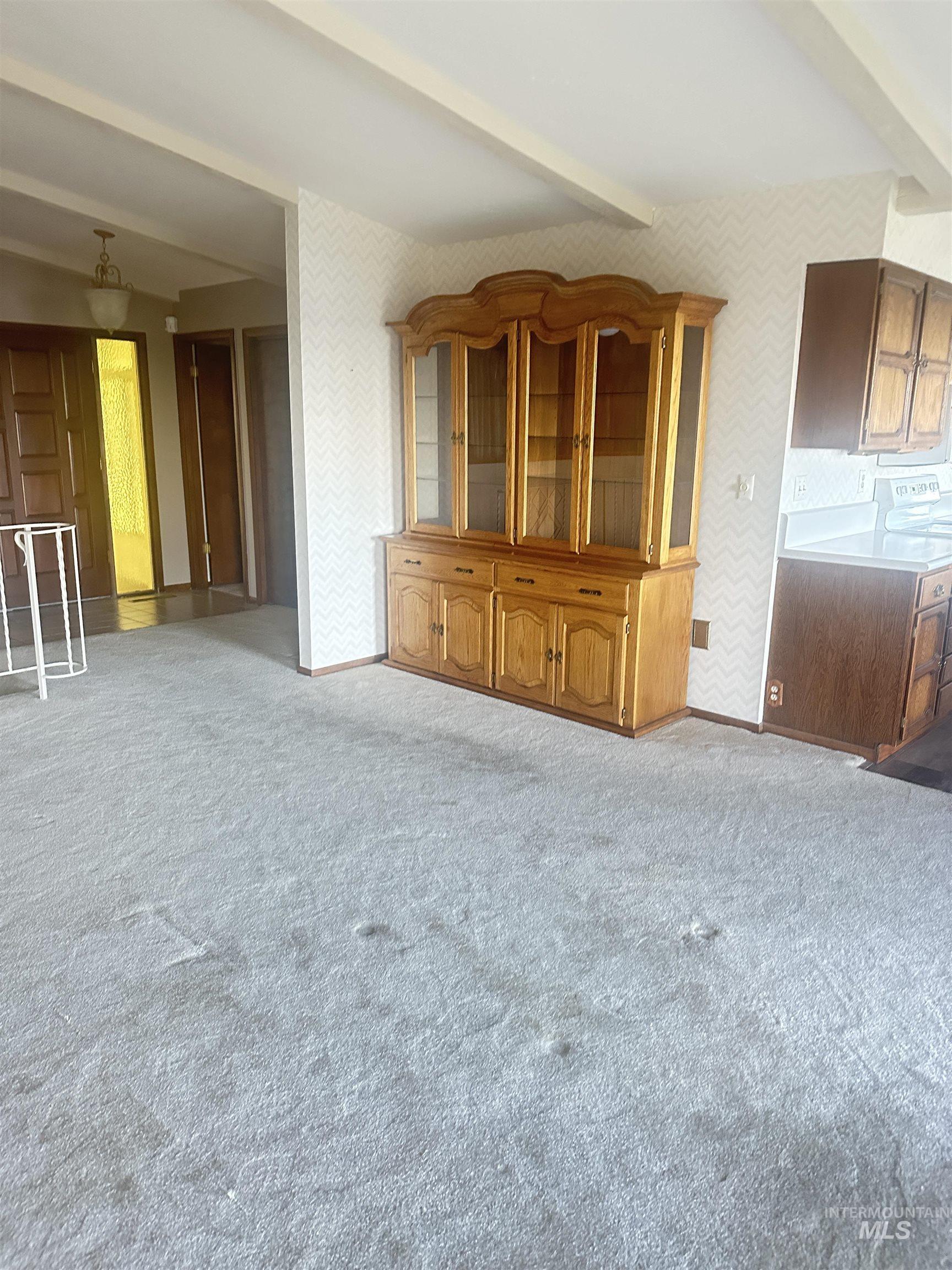 Unfurnished living room featuring beamed ceiling and carpet floors