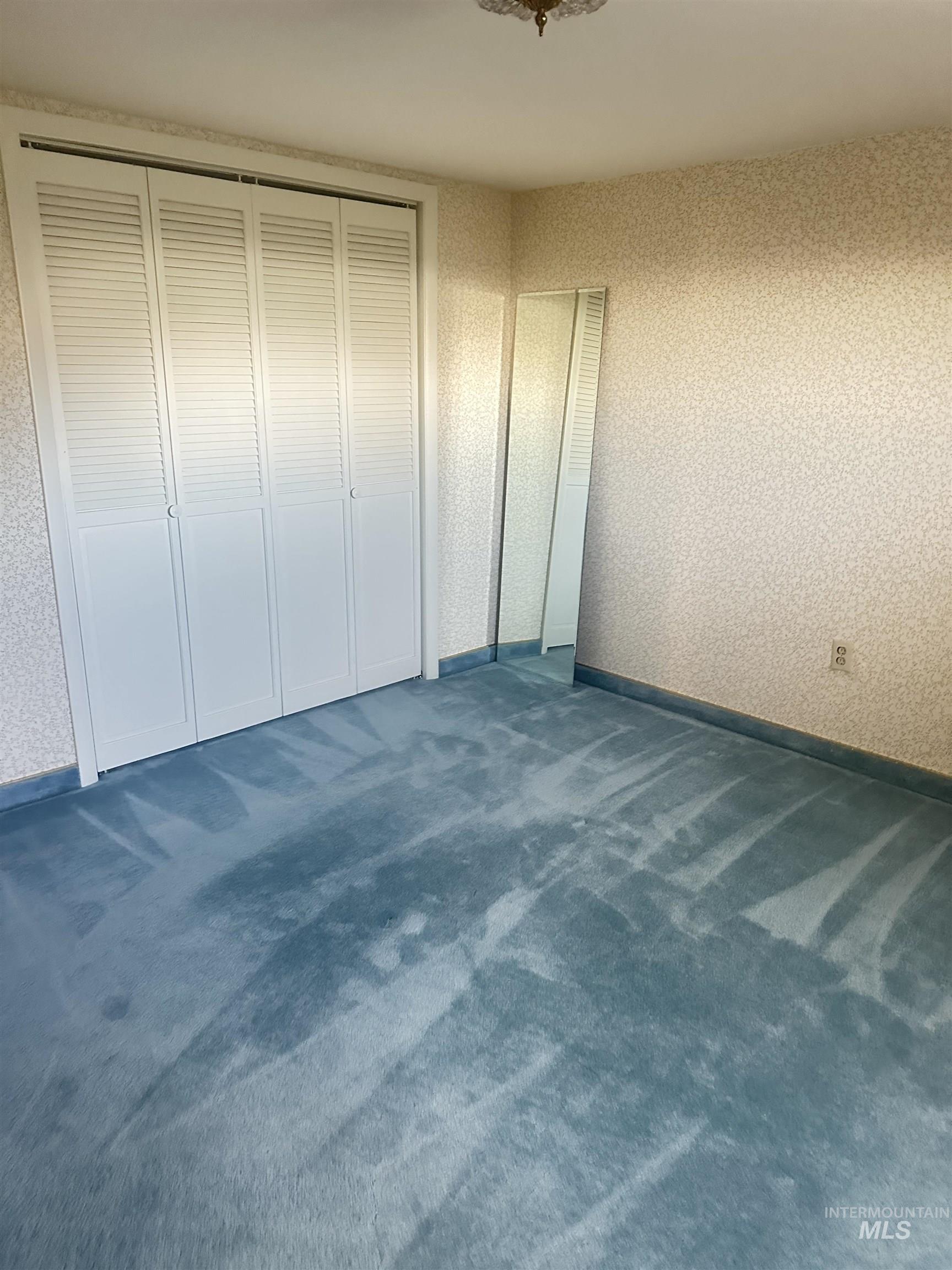 Unfurnished bedroom with wallpapered walls, dark colored carpet, and a closet
