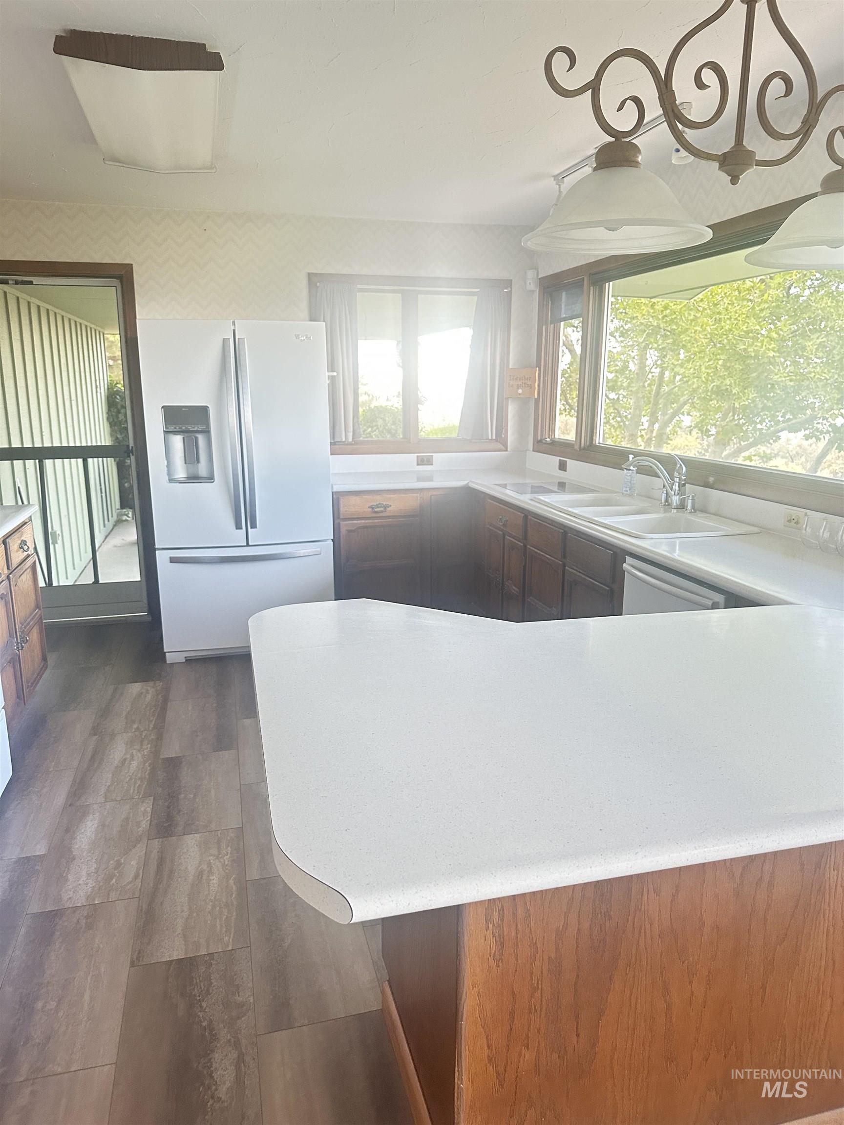 Kitchen featuring fridge with ice dispenser, light countertops, dark wood-type flooring, and healthy amount of natural light