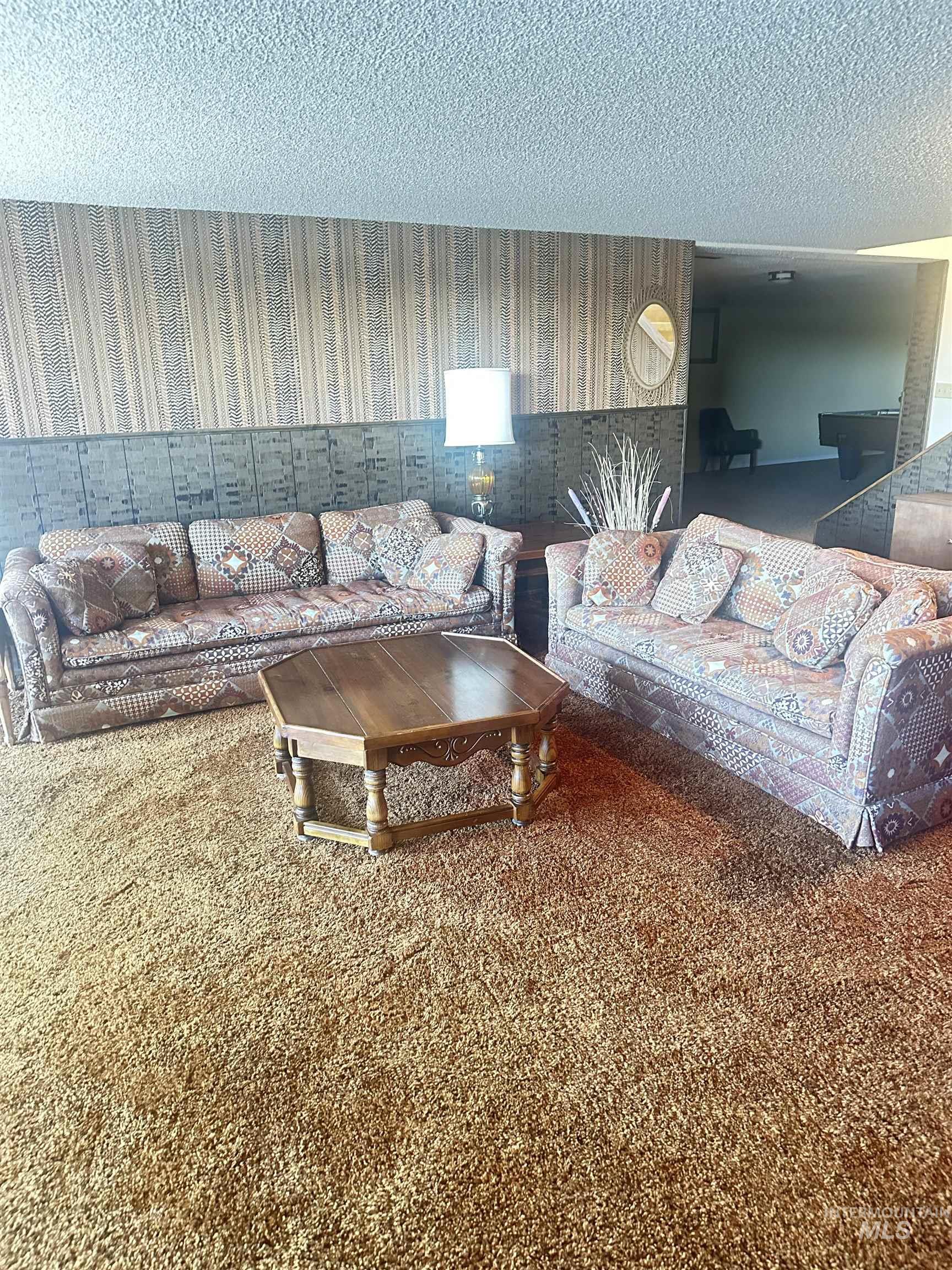 Carpeted living room featuring wallpapered walls and a textured ceiling