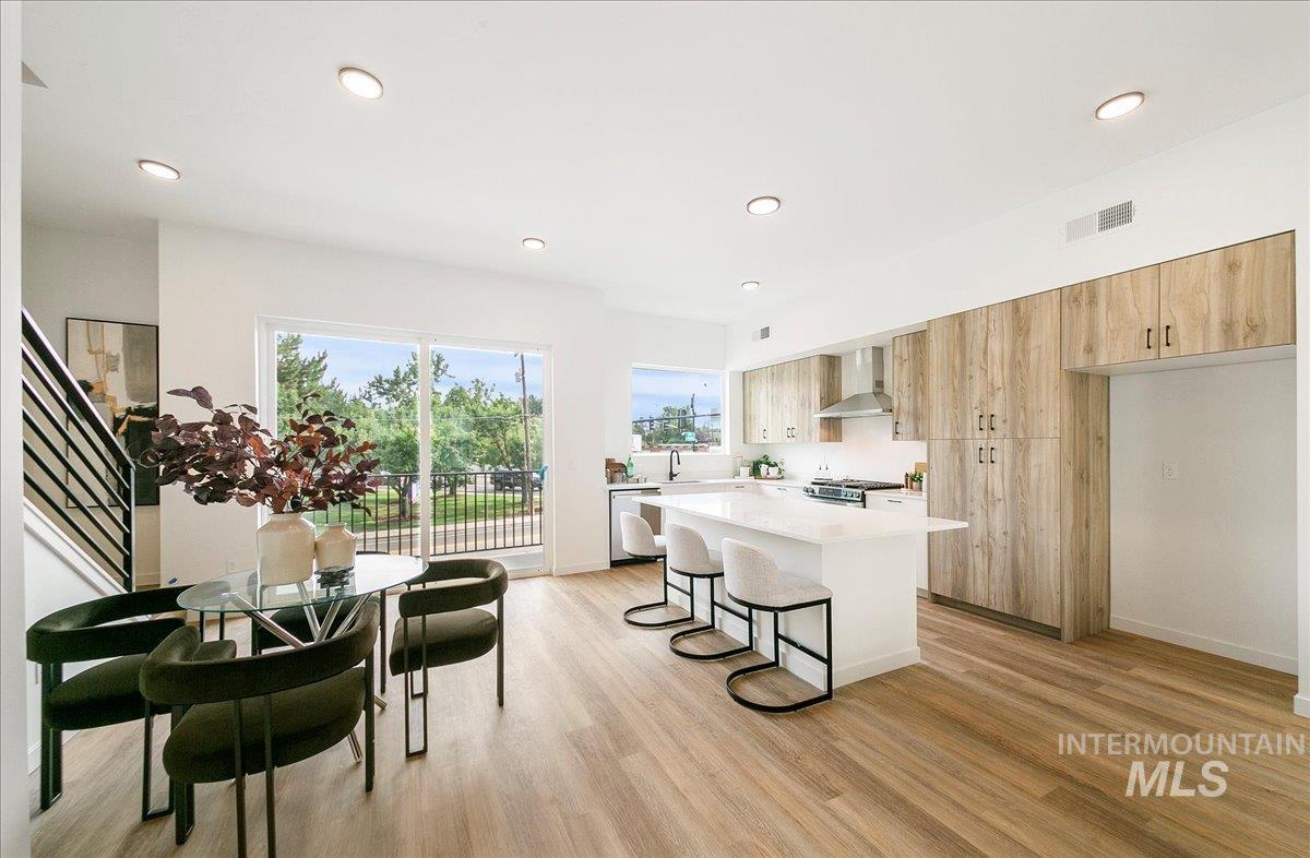 Kitchen featuring modern cabinets, light brown cabinets, a kitchen breakfast bar, light wood-style flooring, and recessed lighting