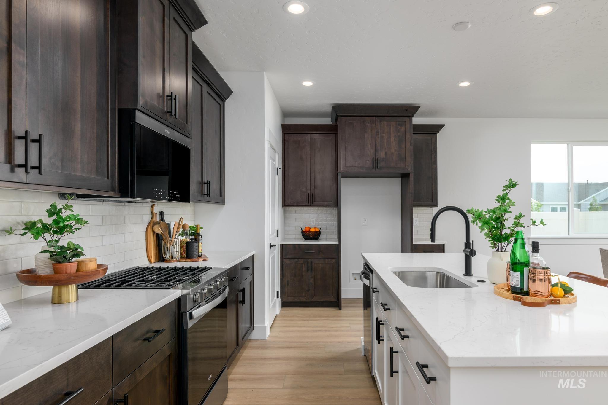 Two tone kitchen with light stone countertops, stainless steel gas range oven, dual tone cabinets, black microwave, and light wood-type flooring