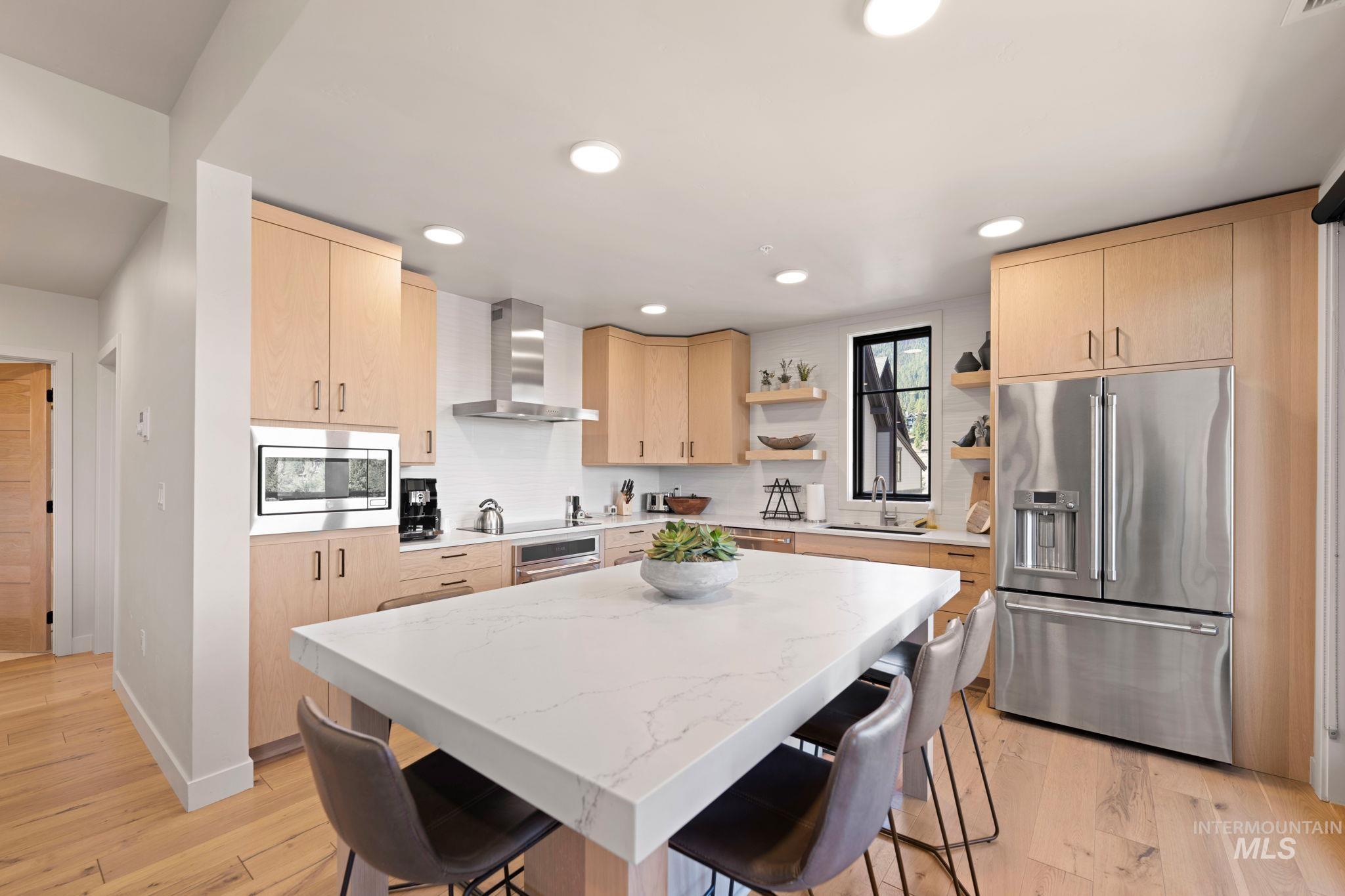 Kitchen with light brown cabinetry, stainless steel appliances, a breakfast bar, light stone countertops, and light wood-type flooring