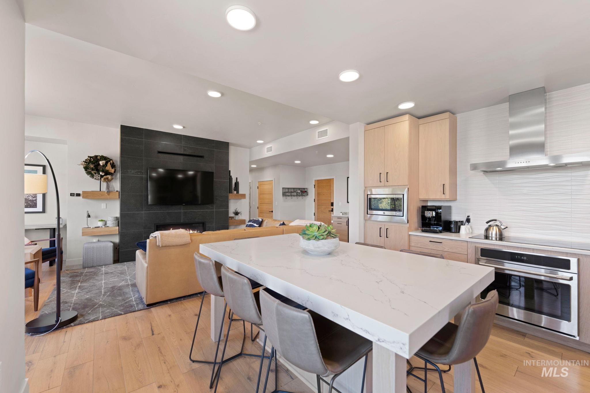 Kitchen with light brown cabinetry, a kitchen bar, wall chimney range hood, stainless steel appliances, and recessed lighting