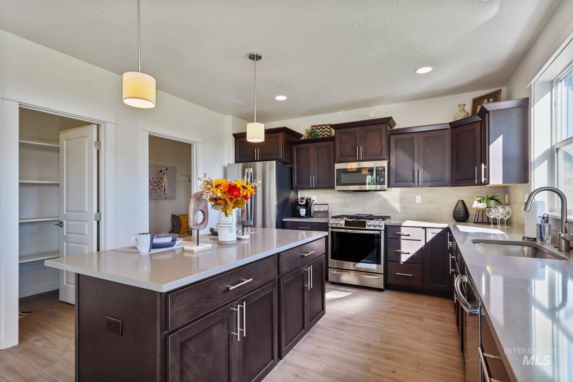 Kitchen featuring dark brown cabinetry, appliances with stainless steel finishes, decorative light fixtures, light wood-style floors, and recessed lighting