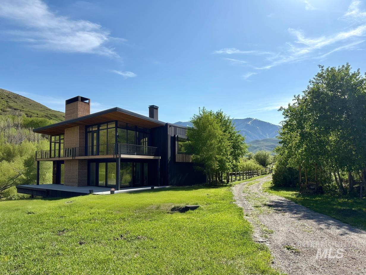Back of house featuring a chimney, a mountain view, a yard, gravel driveway, and a balcony