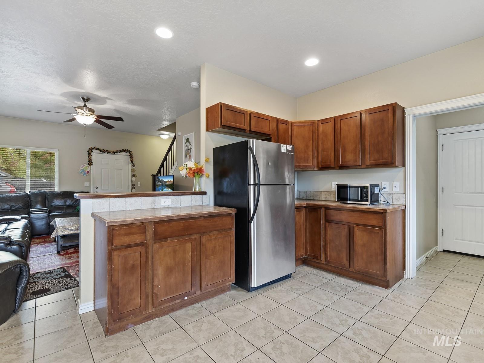 Kitchen with appliances with stainless steel finishes, light tile patterned flooring, brown cabinetry, open floor plan, and ceiling fan