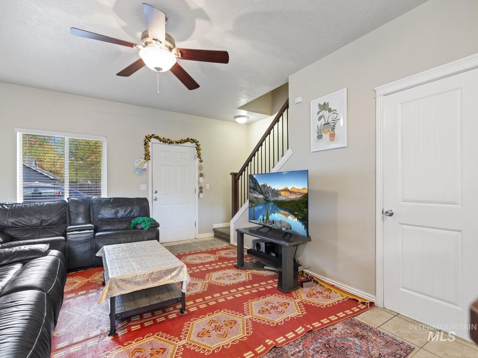 Living area with stairway, light tile patterned flooring, a ceiling fan, and a textured ceiling